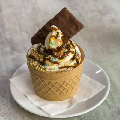 Ice cream dessert in wafer cup with chocolate cookies and creative decoration topping on blurred light copy space background.